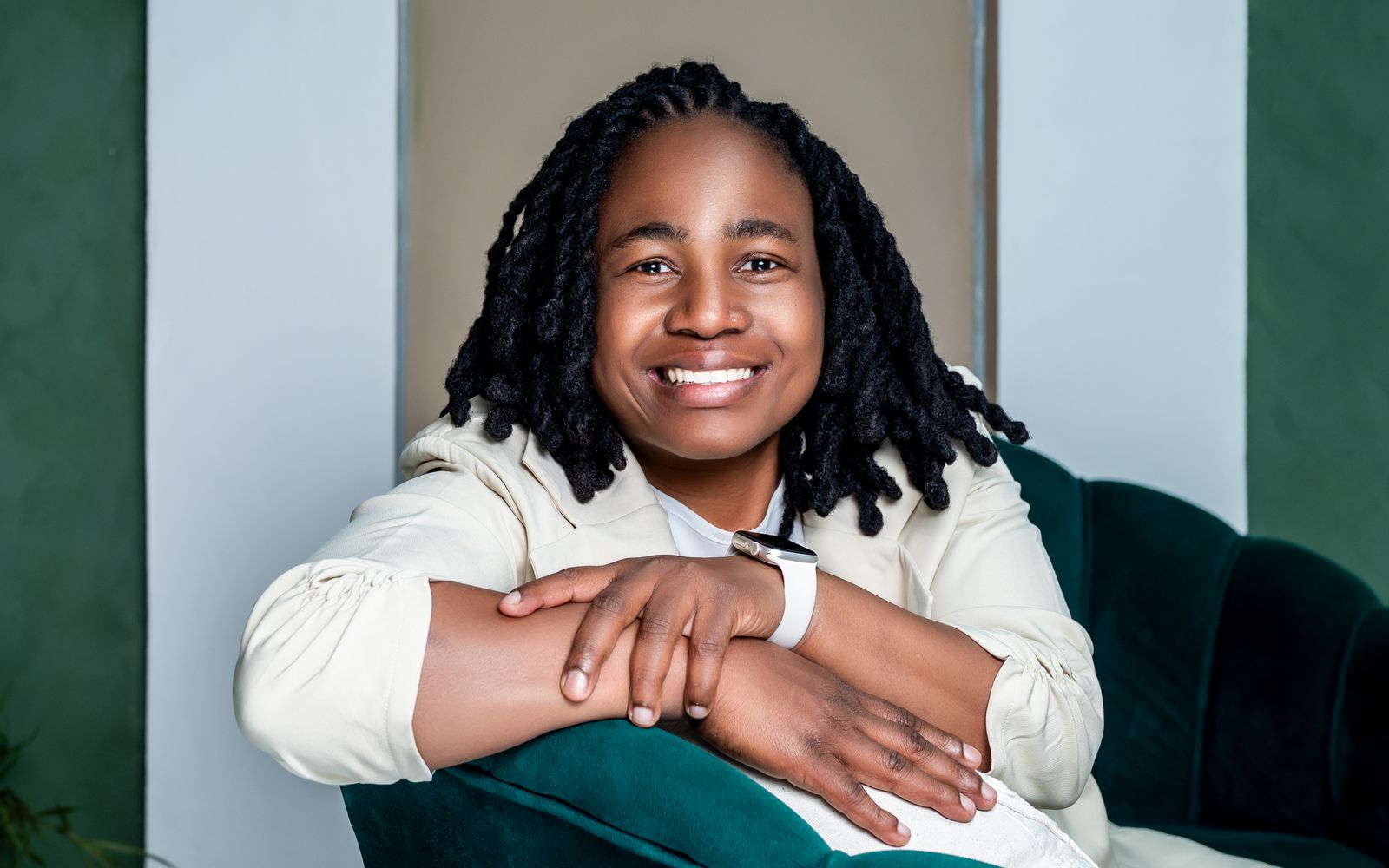 Thembi Buthelezi smiling, seated in a cream suit on a green velvet chair
